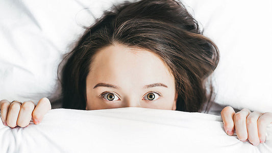 Woman lying in bed with the sheets pulled over her nose and mouth