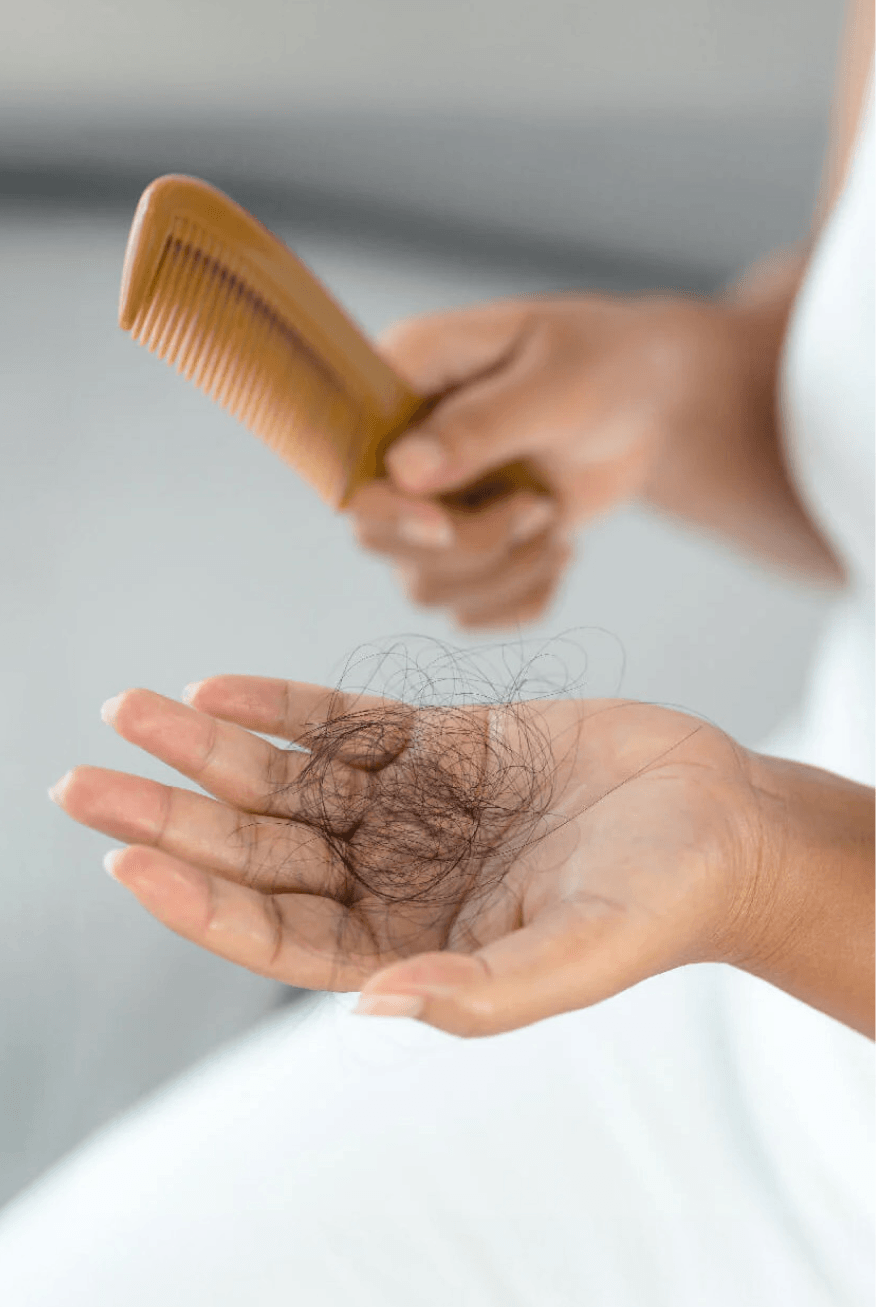 Person holding a comb with hair falling onto their palm, against a neutral background