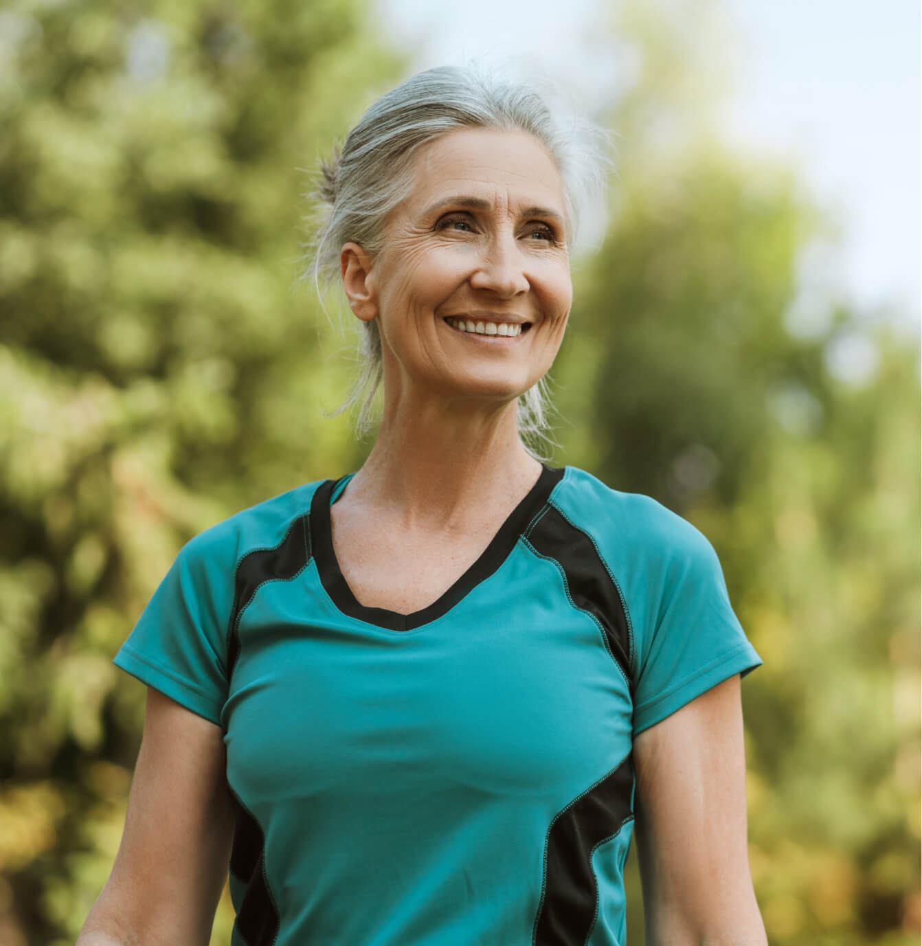 Woman in a teal athletic shirt standing outdoors with greenery in the background