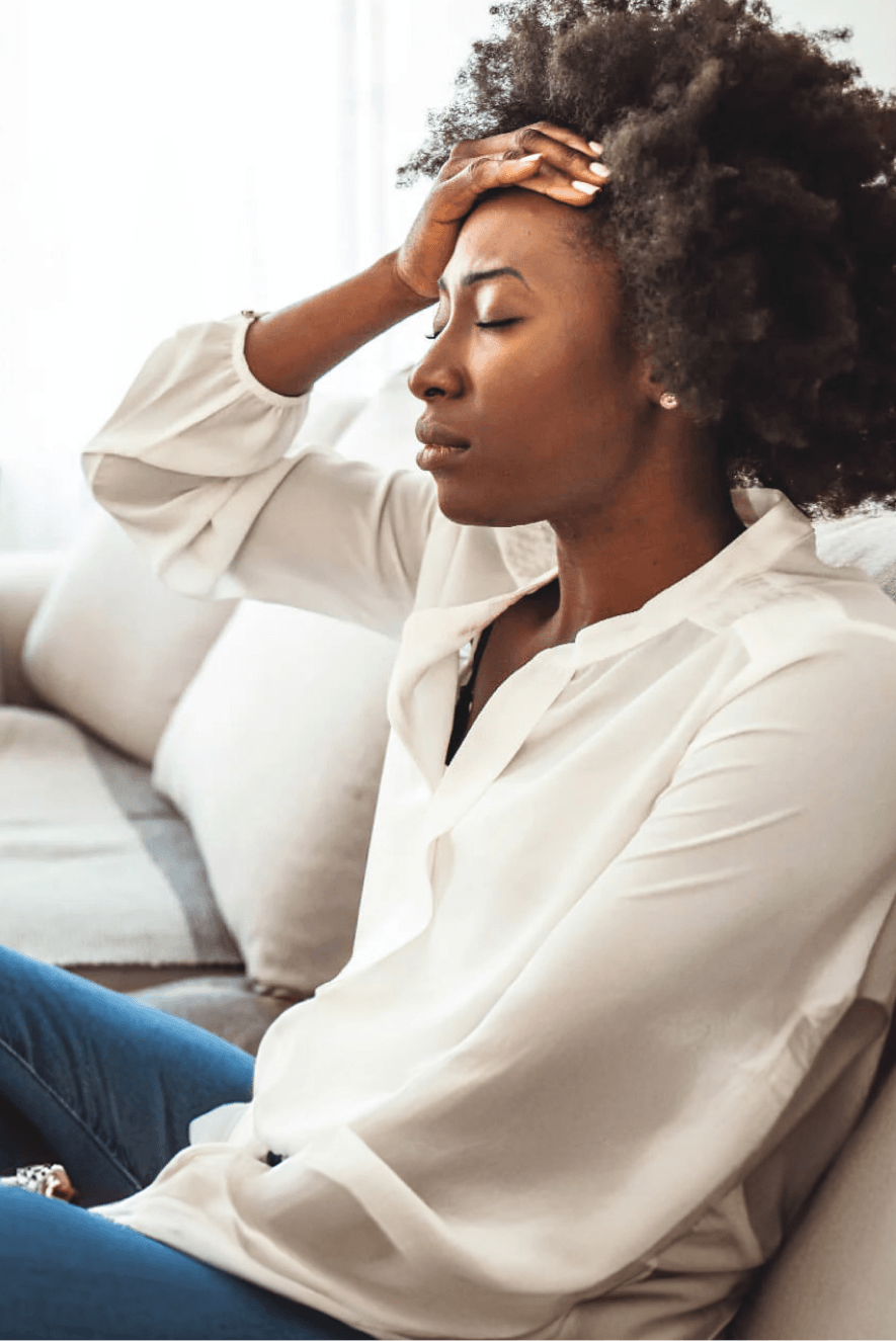 Woman sitting on a couch with her head in her hand, appearing stressed or tired.