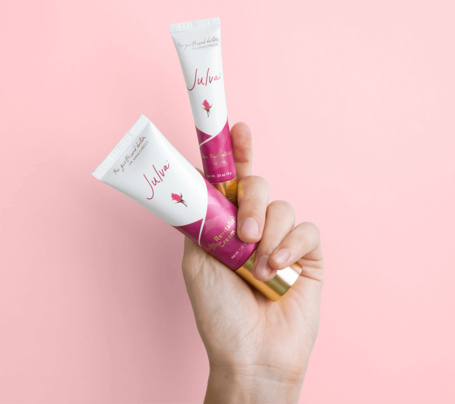 A hand holding two white and magenta tubes of Julva hand cream against a solid pink background.