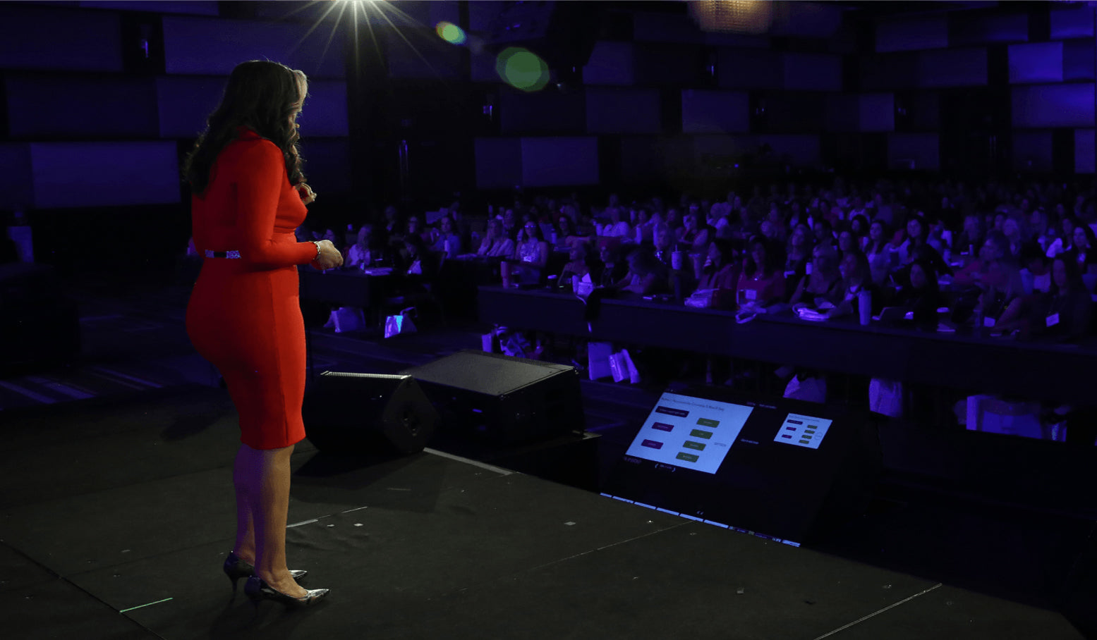 Dr. Anna Cabeca in red dress standing on a stage in front of an audience with purple lighting.