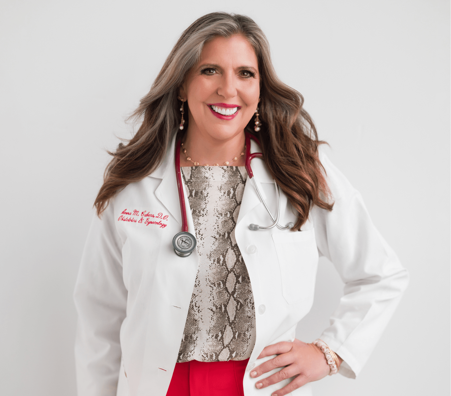 Dr. Anna in a white medical coat with a stethoscope, wearing a patterned top and red pants on a light gray background